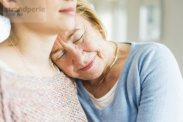 Seniorenfrau mit geschlossenen Augen  die sich gegen die Schulter der jungen Frau lehnt.
