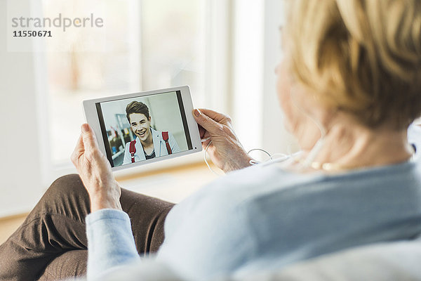 Seniorin betrachtet Bild eines jungen Mannes auf digitalem Tablett