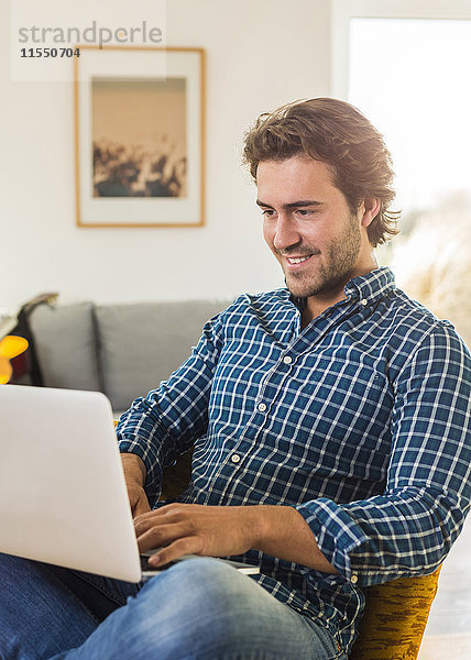 Porträt des lächelnden jungen Mannes im Wohnzimmer mit Laptop