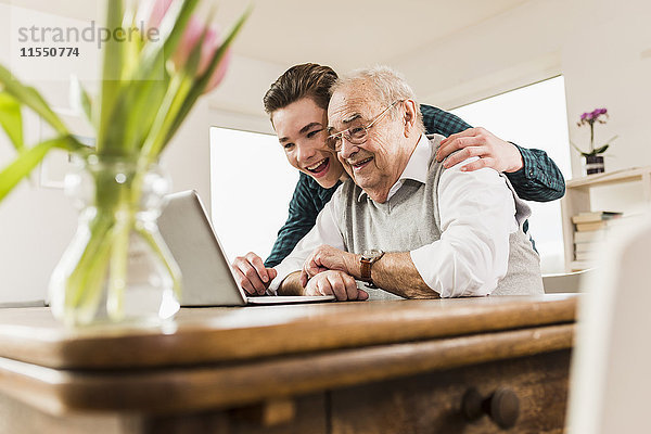 Senior Mann und sein Enkel schauen gemeinsam auf den Laptop im Wohnzimmer