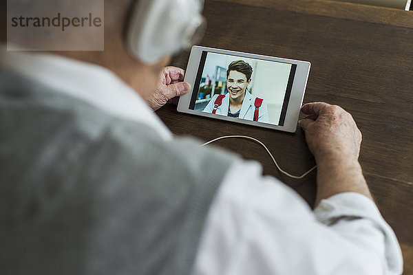 Senior Mann mit Mini-Tablett und Kopfhörer für Skyping mit seinem Enkel