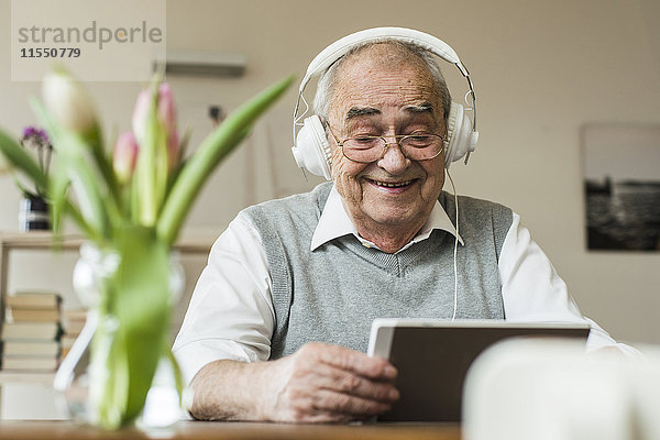 Senior Mann mit Mini-Tablett und Kopfhörer für das Skyping zu Hause