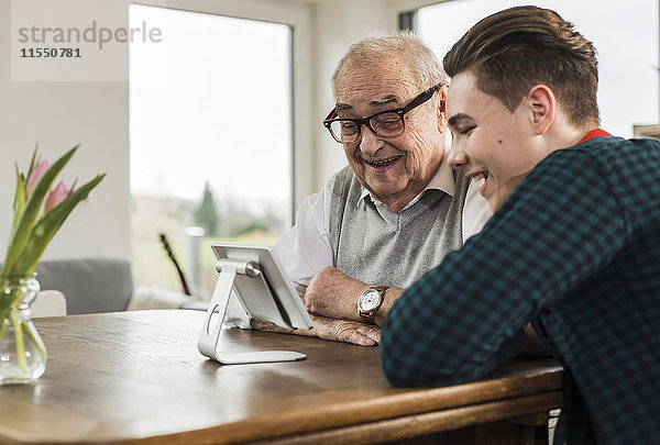 Glücklicher älterer Mann und sein Enkel schauen auf Mini-Tablette