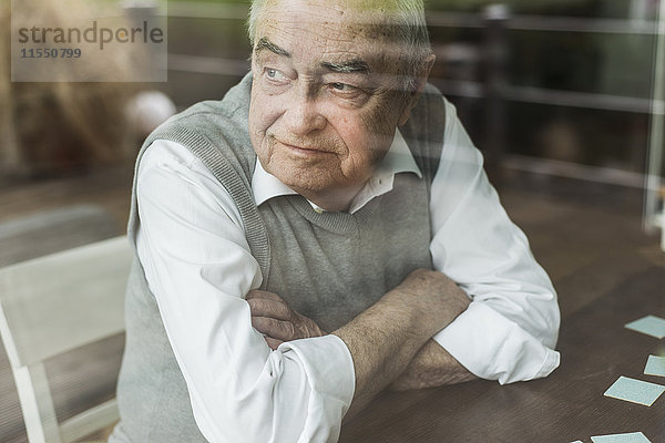 Porträt eines älteren Mannes mit verschränkten Armen  der durchs Fenster schaut.