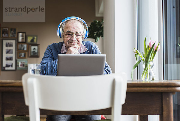 Senior Mann mit Laptop und Kopfhörer zu Hause