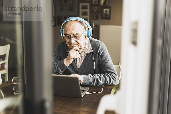 Senior Mann mit Laptop und Kopfhörer zu Hause