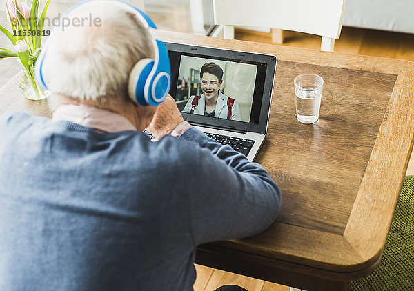 Senior Mann mit Laptop und Kopfhörer für Skyping mit seinem Enkel