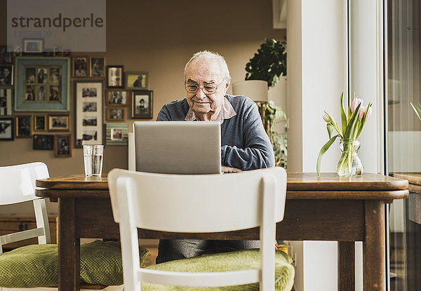 Senior Mann sitzt am Tisch im Wohnzimmer mit Laptop