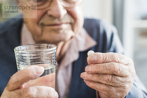 Hände des älteren Mannes halten Tablette und Glas Wasser  Nahaufnahme