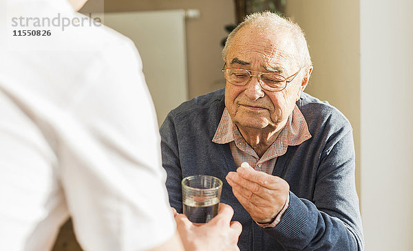 Älterer Mann bekommt Tablette und Glas Wasser