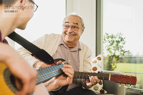Porträt eines älteren Mannes  der mit seinem Enkel Gitarre spielt.