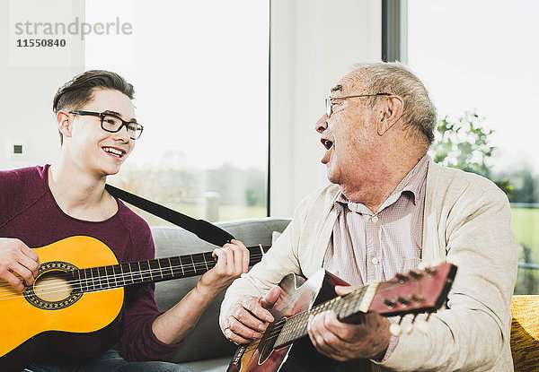 Älterer Mann singt und spielt Gitarre mit seinem Enkel.