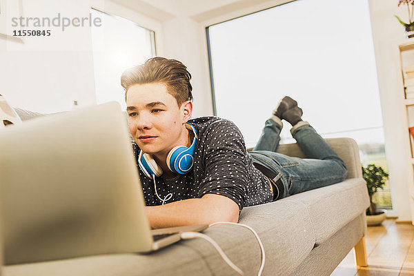 Junger Mann auf der Couch liegend mit Laptop