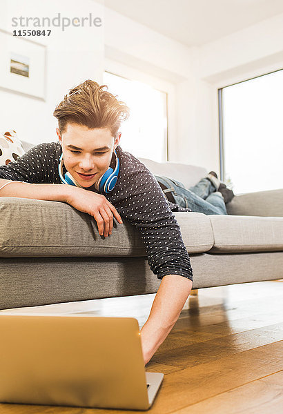 Junger Mann auf der Couch liegend mit Laptop