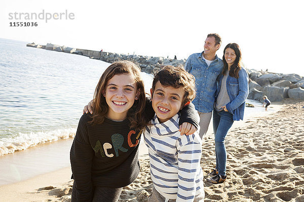 Spanien  Barcelona  Porträt der glücklichen Geschwister am Strand mit ihren Eltern im Hintergrund