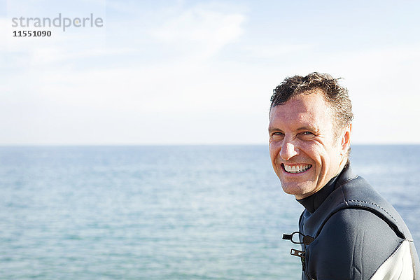 Porträt eines lächelnden Mannes im Neoprenanzug am Meer