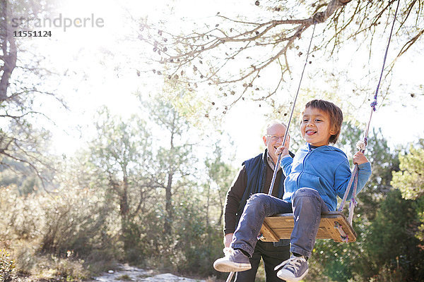 Spanien  Siurana  kleiner Junge  der sich auf einer Schaukel amüsiert  während sein Großvater ihn beobachtet.