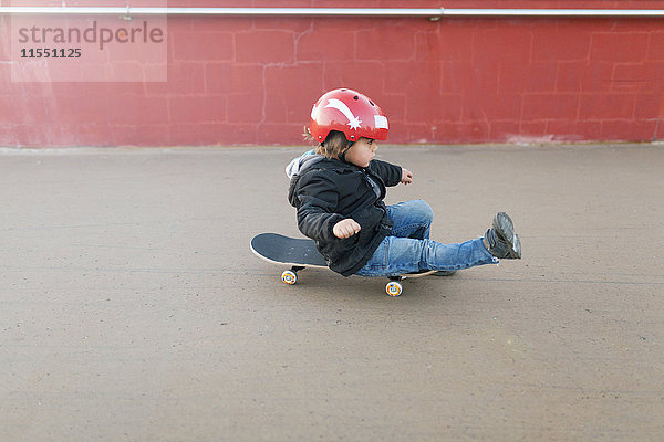 Kleiner Junge mit Schutzhelm auf einem Skateboard sitzend