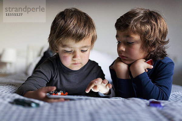 Zwei kleine Jungen liegen auf dem Bett und spielen mit einem digitalen Tablett.