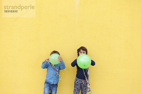 Zwei kleine Jungen mit grünen Luftballons und Luftschlangen stehen vor der gelben Wand