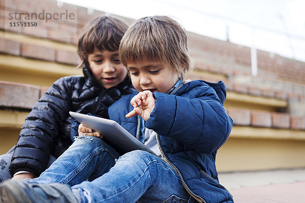 Porträt eines kleinen Jungen  der mit einem digitalen Tablett spielt  während sein Bruder zuschaut.