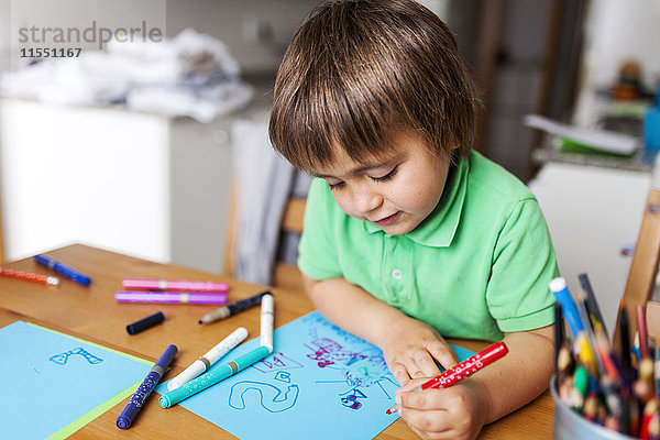 Kleiner Junge malt zu Hause auf blauem Papier
