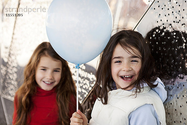 Porträt des lachenden Mädchens mit Ballon und Schwester im Hintergrund