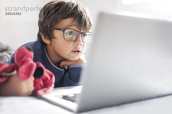 Porträt des kleinen Jungen mit übergroßer Brille beim Blick auf den Laptop
