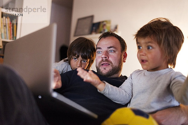 Vater und seine zwei kleinen Söhne schauen sich das Video auf dem Laptop zu Hause an.