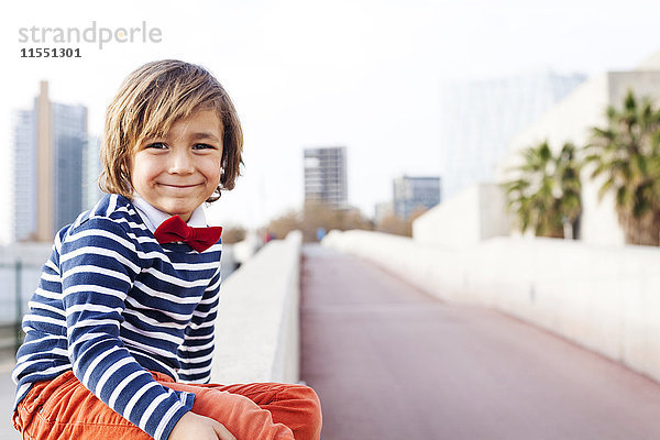Spanien  Barcelona  Portrait eines fröhlichen kleinen Jungen mit Fliege an der Wand sitzend