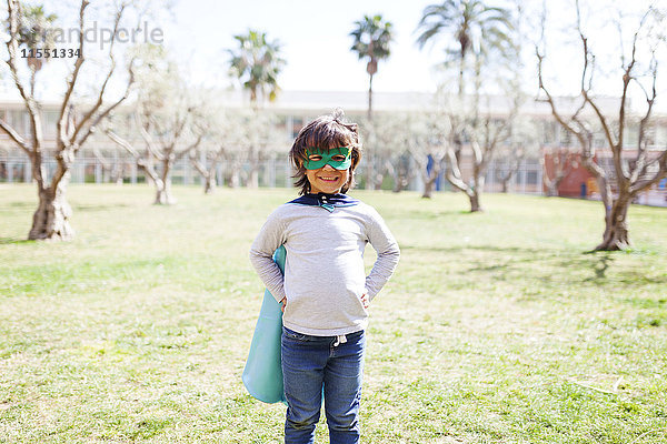 Porträt eines grinsenden kleinen Jungen  verkleidet als Superheld auf einer Wiese stehend.