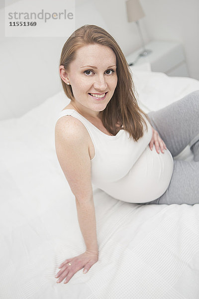 Porträt einer lächelnden Schwangeren auf dem Bett