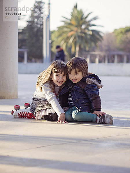 Spanien  Girona  lächelnder kleiner Junge und Mädchen nebeneinander auf dem Boden sitzend