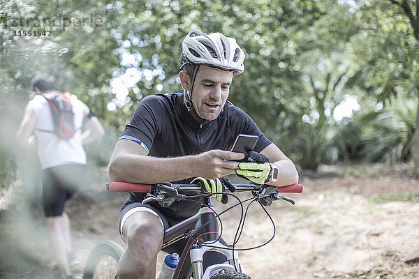 Mann auf dem Mountainbike im Wald mit Blick auf das Handy