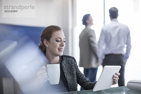 Lächelnde Frau im Büro mit einer Tasse Kaffee und einem digitalen Tablett