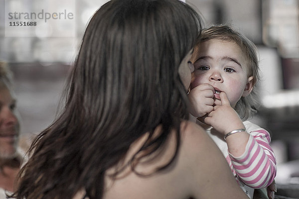 Porträt des Mädchens mit Finger im Mund auf den Armen ihrer Mutter