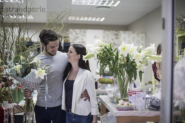Glückliches junges Paar mit Blumenstrauß verlässt den Blumenladen
