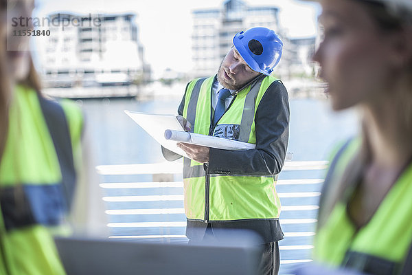 Ingenieur auf der Baustelle mit Blaupause  Telefongespräch