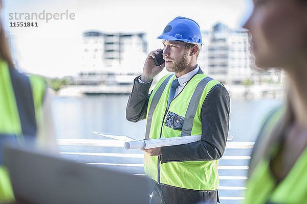 Ingenieur auf der Baustelle mit Blaupause  Telefongespräch