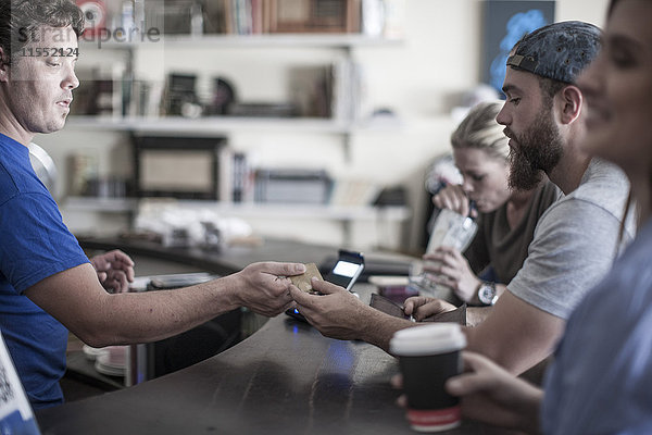 Junger Mann bezahlt mit Kreditkarte im Café