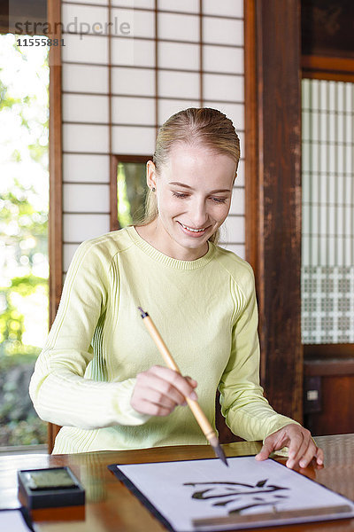 Kaukasische Frau übt Kalligraphie in einem traditionellen japanischen Haus