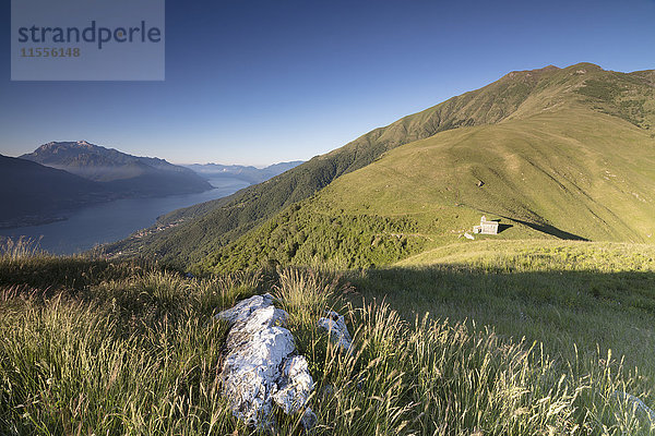 Sonnenstrahl auf der Kirche von San Bernardo beleuchtet die Landschaft um das blaue Wasser des Comer Sees in der Morgendämmerung  Musso  Lombardei  Italien  Europa