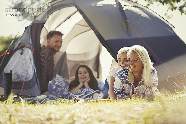 Lächelnde Familie entspannt vor dem sonnigen Zelt auf dem Campingplatz