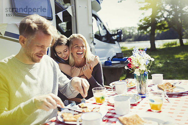 Fröhliche Familienumarmung und Frühstück vor dem sonnigen Wohnmobil