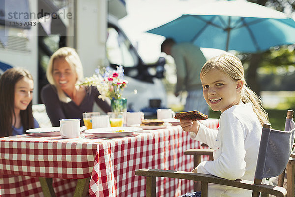 Portrait lächelndes Mädchen beim Frühstücken mit der Familie vor dem sonnigen Wohnmobil