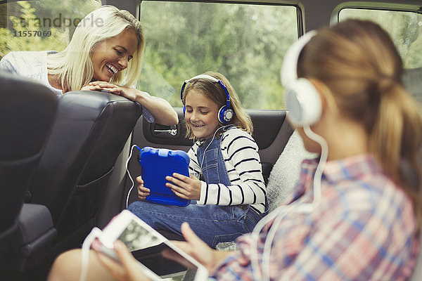 Mutter beobachtet Töchter mit Kopfhörern und digitalen Tabletts auf dem Rücksitz des Autos