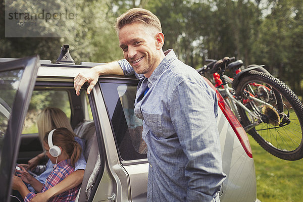 Portrait lächelnder Vater auf dem Auto mit Mountainbikes