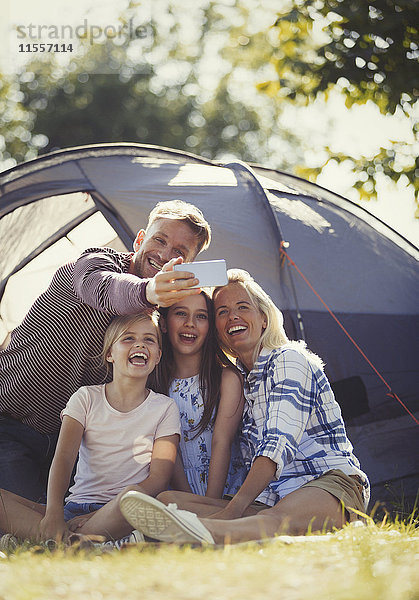 Glückliche Familie nimmt Selfie mit Fotohandy außerhalb des sonnigen Zeltplatzes.