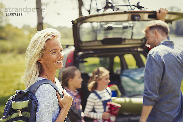 Lächelnde Frau mit Rucksack zur Vorbereitung der Wanderung mit der Familie außerhalb des Autos