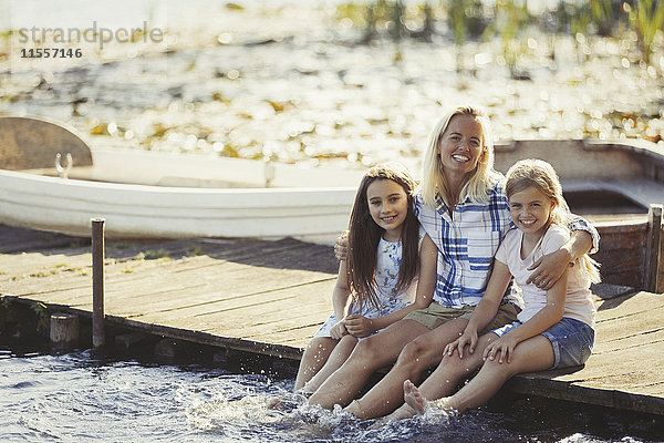 Portrait glückliche Mutter und Töchter auf Dock spritzende Füße im See